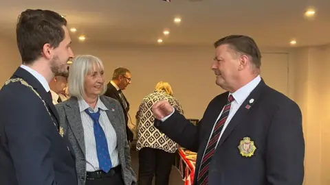 Thomas Murray, Dr Lori Boul and councillor Kevin Foster stand talking to each other in a room