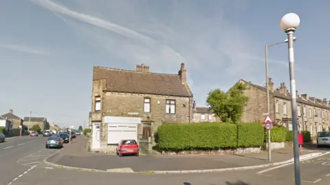 A view of an end-terrace property with the corner house converted into a shop front. There is one car parked directly outside and some on the street too.