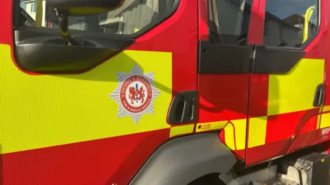 A Devon and Somerset Fire and Rescue Service truck. It has yellow and red blocks with a fire badge on the door.