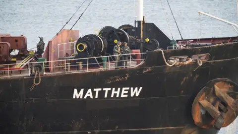 Black boat with Matthew in white text, military personnel pictured onboard deck