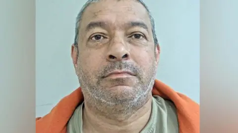 Michael Harvey's mugshot. He has short cropped salt and petter hair and stubblee, brown eyes, and is wearing an orange fleece over a pale green tshirt
