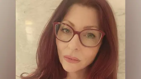 Teana Lynne has long red hair and red-framed glasses in this selfie.