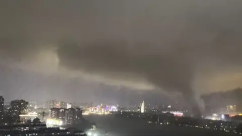 A giant tornado sweeping a city in the night, with the skyline of a city behind it