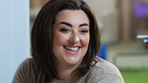 Bianca Perea with long brown hair smiling wearing a beige long sleeved t-shirt