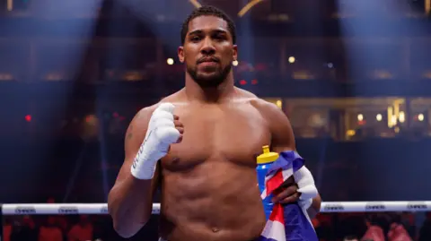 Reuters Anthony Joshua raising a fist with a smile at the camera while stood in a boxing ring