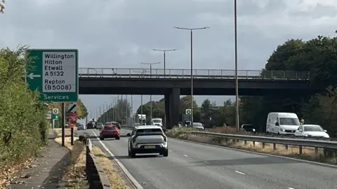 Cars travelling on a dual-carriageway with a bridge in the background.
