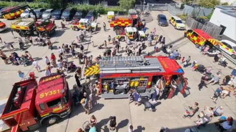 Surrey Fire and Rescue Service Aerial shot of a fire service open day, with people milling around an assortment of fire engines in a large concreted area.
