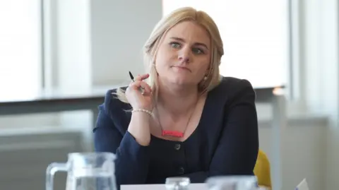 PA Media A mid shot of Alex Davies-Jones in a meeting. She has long blonde hair and is wearing a navy top. She is holding a pen and looks focused on the conversation.