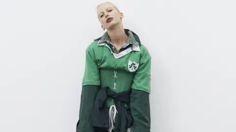 Pierre Toussaint A woman with blonde hair wearing a green corset Ireland rugby shirt