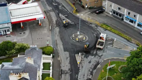 A petrol station forecourt sits next to the roundabout, where a works vehicle can be seen parked across the roundabout.