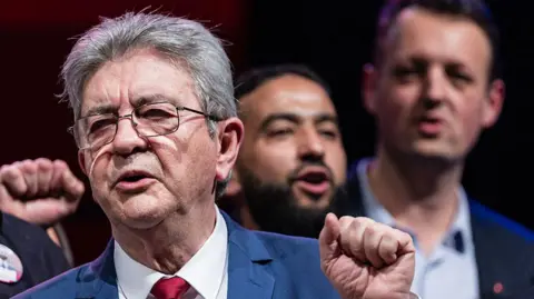 AFP via Getty Images A man holds up his fist wearing glasses and a light blue suit