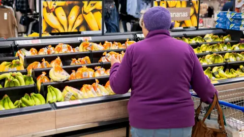 A woman in a purple jumper shops for bananas in a supermarket in the UK