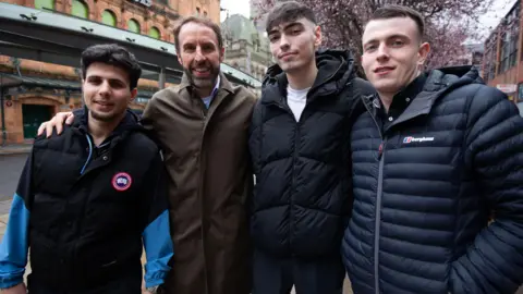 Sir Gareth Southgate stands with three young men. His arms are round the two closest to him