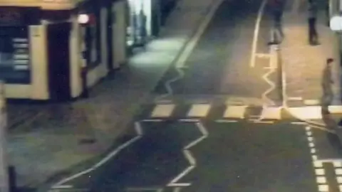 Suffolk Police A grainy CCTV image showing a man walking onto a pavement having walked over a zebra crossing. 