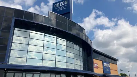 James Grant/BBC The outside of the cinema. It has curved reflective glass on the front and a sign above it