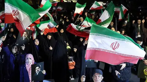 People wave national flags and hold portraits of Iran's supreme leader Mojtaba Khamenei as they march in support of the Iranian armed forces in central Tehran on March 25, 2026.