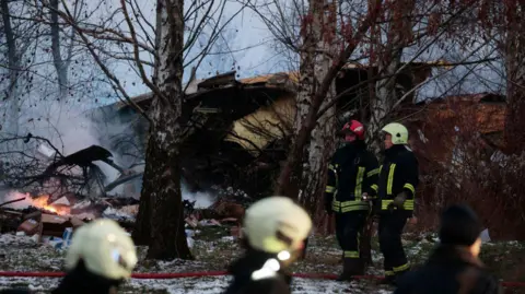 AFP via Getty Images Wreckage of a crashed plane with emergency services staff at the scene