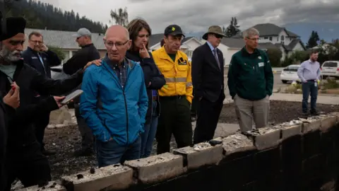 Reuters Jasper Mayor Richard Ireland, looks at what is left of his home of 67 years with federal Minister of Emergency Preparedness Harjit Sajjan, Premier Danielle Smith, and Minister of Forestry and Parks Todd Loewen in Jasper, Alberta, Canada, on Friday, July 26, 2024. AMBER BRACKEN/Pool via REUTERS