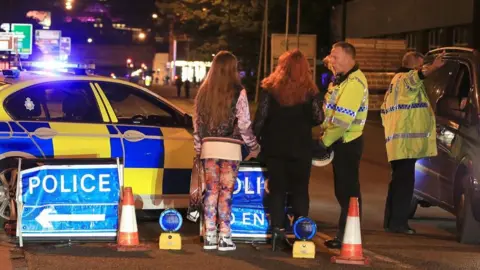 Peter Byrne/PA Wire Two police officers stand in a road near Manchester Arena on the night of the bombing. One officer is speaking with a woman and a girl who are holding hands. The other officer is directing the driver of a car.