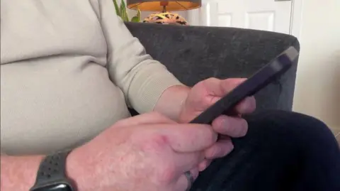 Phil Bodmer/ BBC A close-up of a man holding a phone.