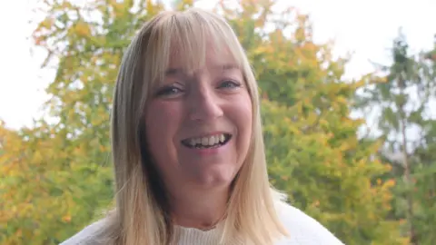 Image of Andrea Warnes smiling at the camera. She has short blonde hair, blue eyes, and is wearing a white jumper. 