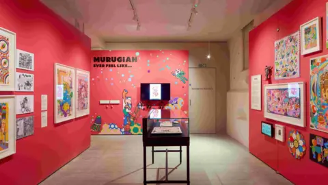 Hufton + Crow Photography Straight shot of a museum room with lots of framed prints on the walls which are painted red and one glass display box in the middle.