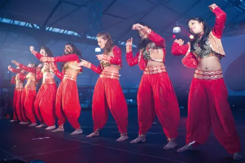 Belfast Mela Seven women in red costumes standing on stage