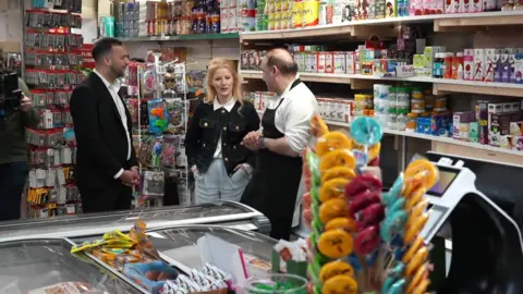 Zack Polanski and Hannah Spencer talk to a shopkeeper inside a shop 