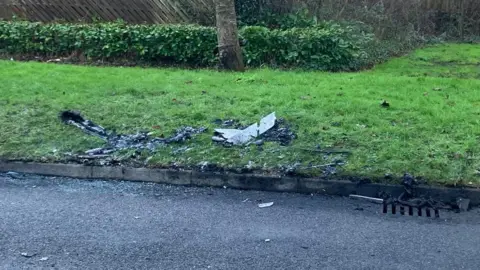 Amy Holmes/BBC An image of discarded parts of the burned out bus on roadside and on a bit of grass on a verge.