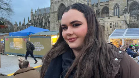 A woman wearing a coat and scarf standing outside a Christmas market in Exeter.