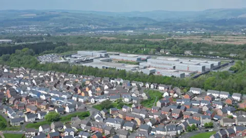 BBC A drone image of Parc Prison, in front of it is the Parc Derwen housing estate can be seen, with hills in the distance behind it 