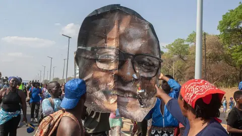 AFP via Getty Images A group of people hold up a giant image of the head of Lazarus Chakwera that has been torn down from a billboard.
