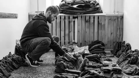 Chris Garrett, a man who has stubble and long light hair is crouched down looking at equipment.