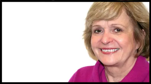 A smiling Helen McDermott looks directly at the camera. She wears a pink sweater and has brown hair.