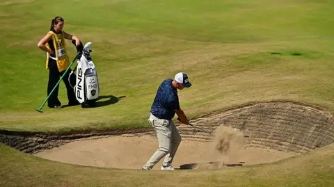 Getty Images A golfer in a navy shirt plays a shot from the bunker.
