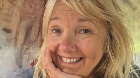 Susan Williams Susan Williams, smiling at the camera, with her chin resting on her palm. She has long blonde hair.
