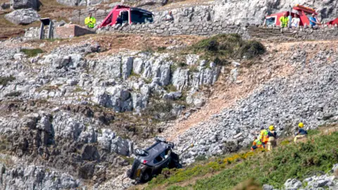 FPNW Crews work to recover the vehicle which is lying upside down and pointing back up the slopes