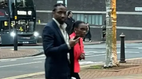 BBC Tai Yasharahyalah, in a black suit, and Naiyahmi Yasharahyalah, in a red jacket, walk to court