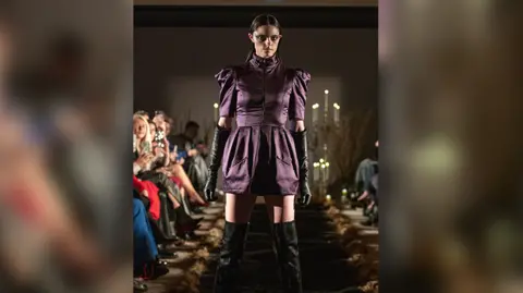 Chris Yates Photography A model on a catwalk wearing a short purple dress surrounded by an audience on either side of her