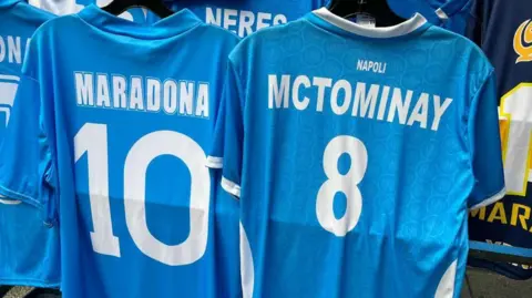 McTominay shirt hanging next to a Maradona shirt outside a shop in Naples