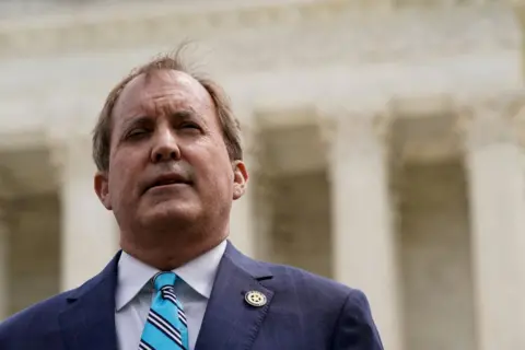 Reuters Head and shoulders shot of Ken Paxton wearing a white shirt and blue striped tie, standing outside US Supreme Court in 2022