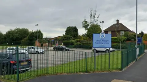 A sign on a fenced off grass verge next to a car park says 'Ditton Primary Academy School'. 