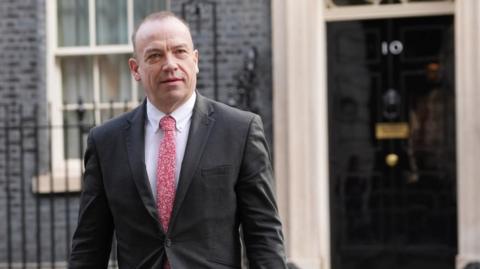 Chris Heaton-Harris with very short dark hair wearing a red patterned tie, outside Downing Street