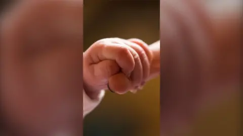 A baby's finger is holding the end of its mother's finger