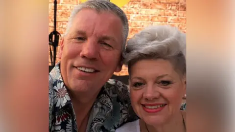 Paul and Beverley Hazell A selfie of Paul and Beverley Hazell. Paul has short grey hair and is wearing a blue floral shirt. Beverley has short grey hair and is wearing a white top.