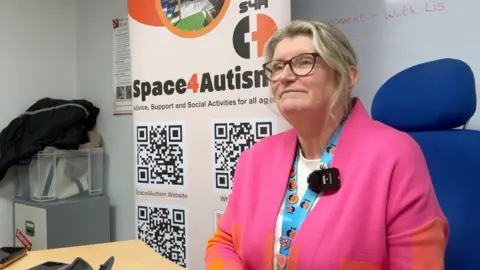 Cheryl Simpson, the chief executive of Space4Autism. She is sat at a desk in front of one of the charity's banners.
