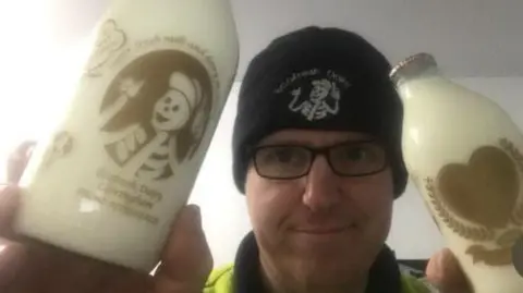 Paul Luke Paul Luke, wearing a hat and glasses, holding two bottles of milk