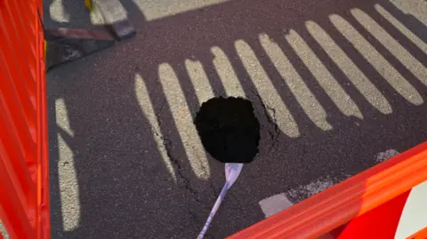 A sinkhole within a cordoned-off area surrounded by red barriers.