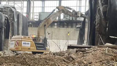 A yellow excavator removing rubble from the turbine hall.