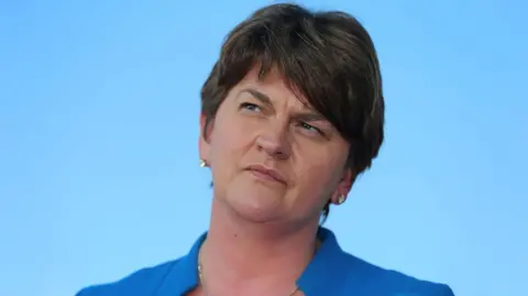 PA Media Arlene Foster stares upwards to her right. She has short dark hair and is wearing a blue suit jacket